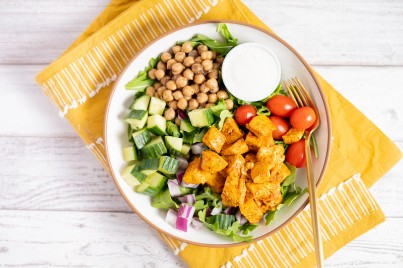 A salad built from the Maven Meals salad bar: arugula, spiced chickpeas, cucumber, cherry tomatoes, red onion and spiced chicken, with a cup of creamy dressing on the side