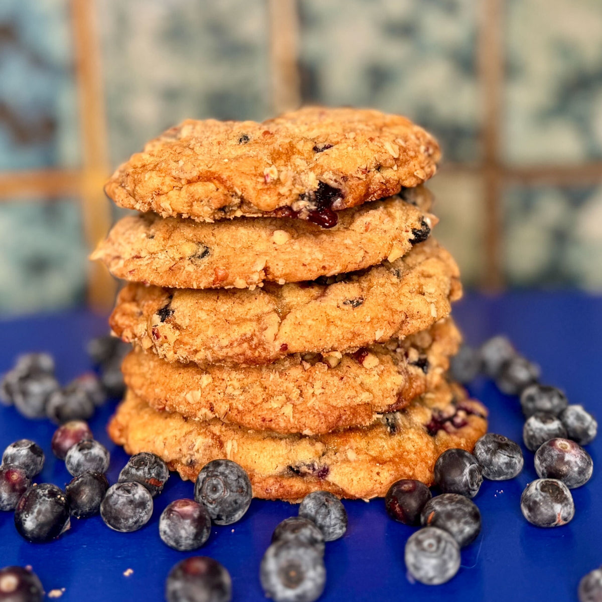 A stack of blueberry streusel cookies on a blue plate with fresh blueberries scattered around.