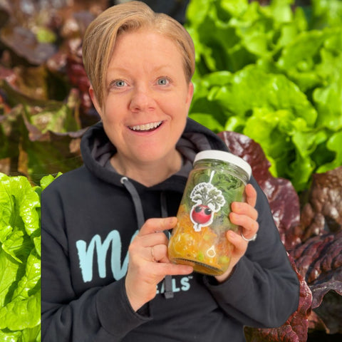 Person holding a jar with a brand logo against a background of leafy greens