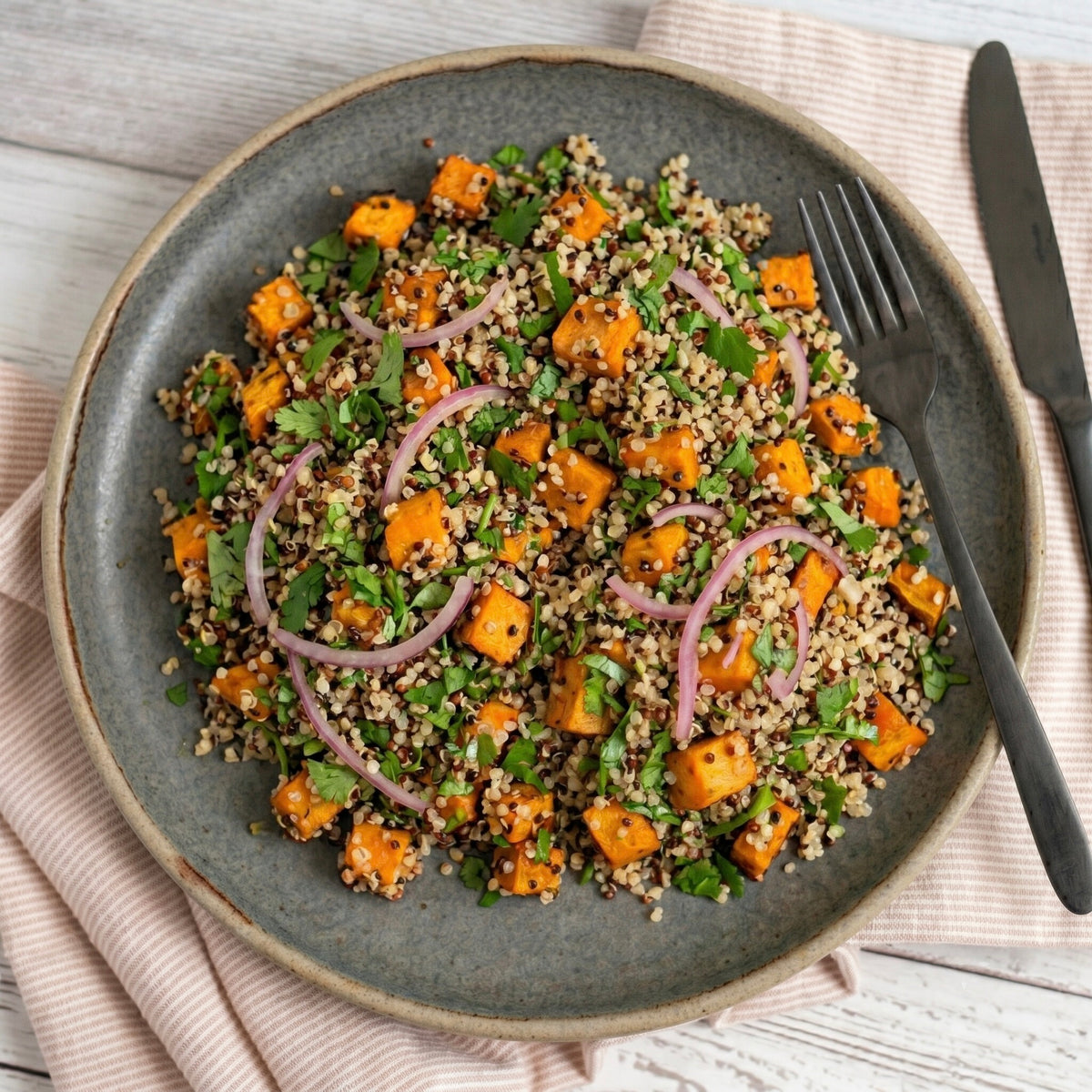 Plated salad with sweet potatoes, quinoa, and vegetables on a wooden table.