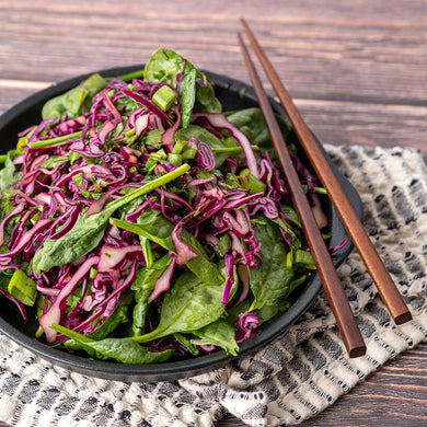 A bowl of Asian Sesame Spinach Slaw with red cabbage and green spinach, accompanied by chopsticks, set on a patterned napkin.