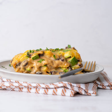 A plate of stacked zucchini and black bean enchiladas with a creamy green enchilada sauce, garnished with chopped herbs, on a striped napkin.