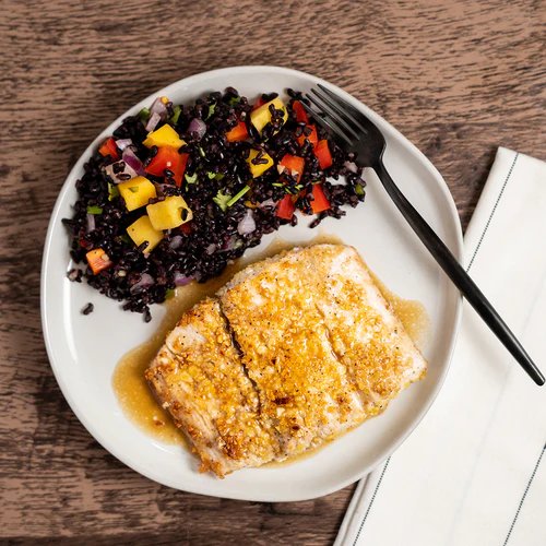 A crusted white fish fillet in pan sauce with black rice and mango salsa