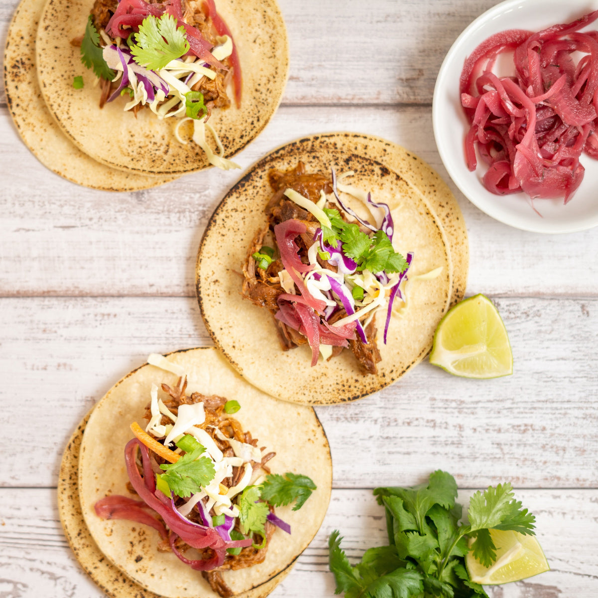 Guajillo beef tacos on corn tortillas with cabbage slaw, pickled red onion and cilantro, with lime wedges alongside