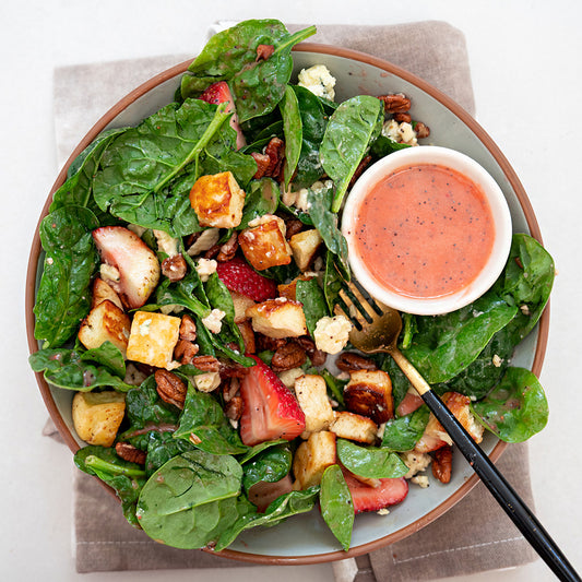 A plate of Halloumi Spinach Strawberry Salad with a side of pecans and strawberry poppyseed dressing.