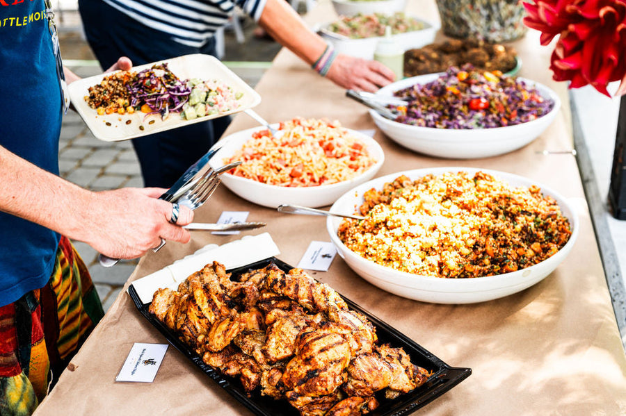 Office lunch catering from Maven Meals: a buffet of grilled chicken thighs, couscous salad, carrot salad and red cabbage slaw, with a guest filling a plate