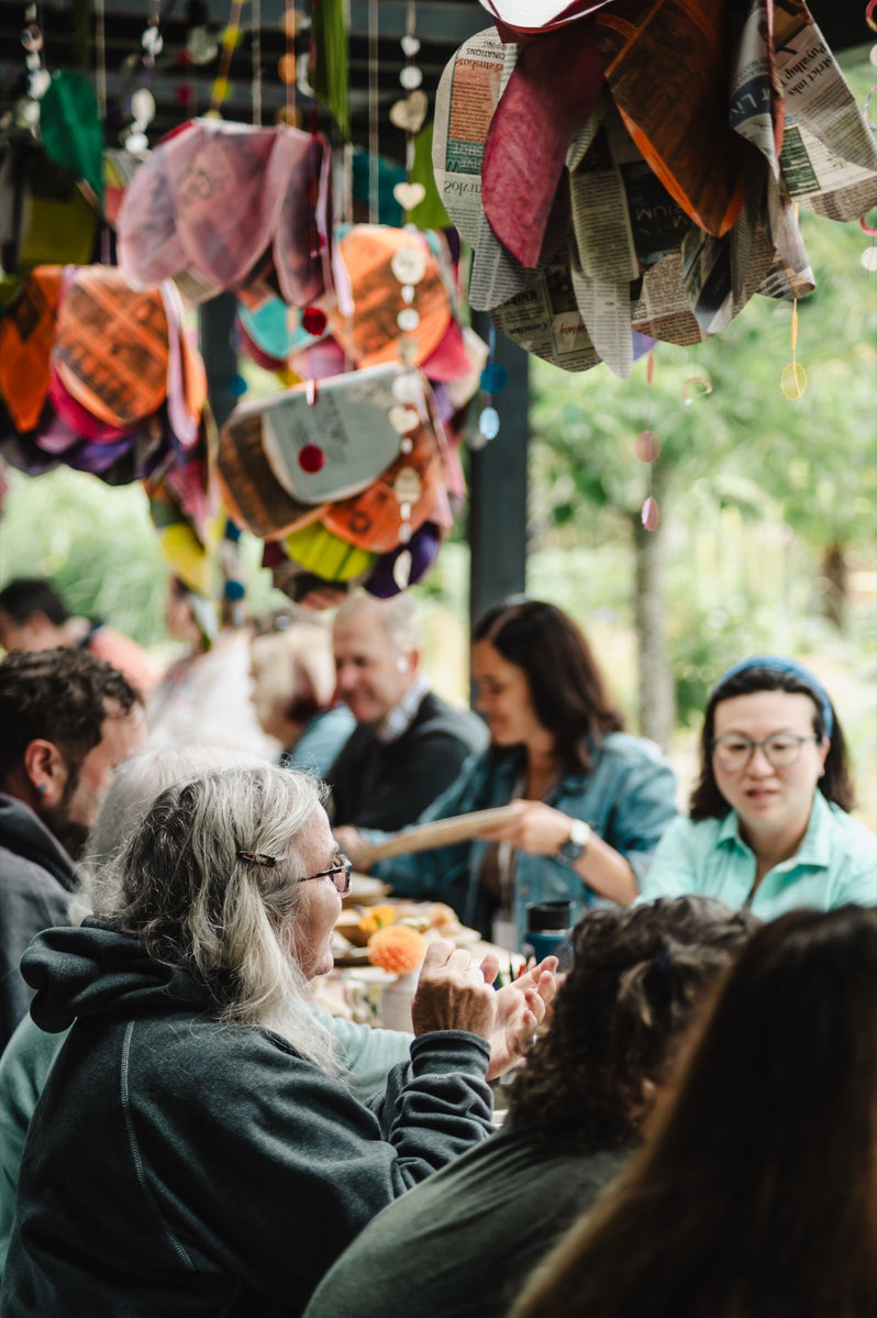 Guests talk over a catered lunch at a long outdoor table under hanging paper lanterns