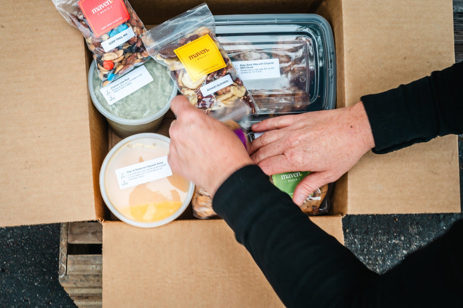Packing a Maven Meals delivery box with labeled containers of soup, cilantro lime rice, ribs, trail mix and a cookie