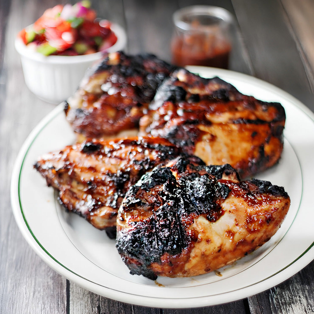 A plate of grilled chicken thighs with a glossy Asian-inspired plum sauce, accompanied by a side of plum salsa.