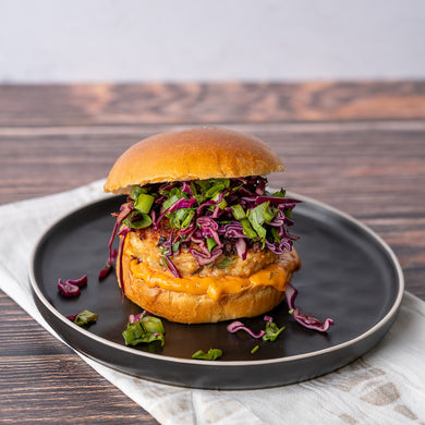 A teriyaki chicken burger with sesame slaw, served in a brioche bun on a dark plate, with a wooden background.