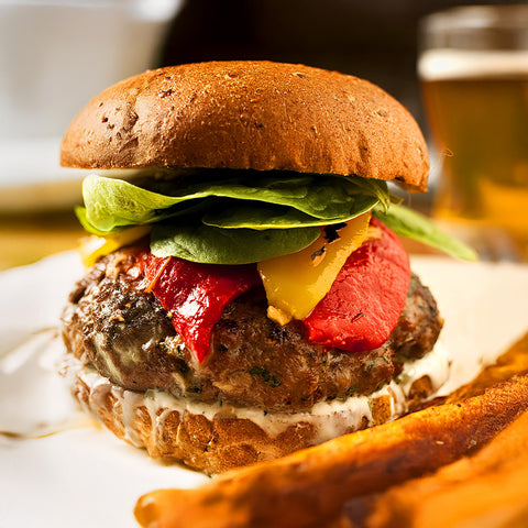 Lamb burger with lettuce, tomato, and cheese on a bun with a side of fries and a drink in the background.