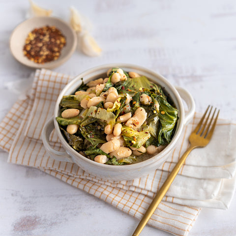 A bowl of garlicky braised escarole with cannellini beans on a table with a striped napkin and a gold fork.