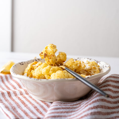 A bowl of roasted cauliflower florets garnished with chermoula, served on a white plate with a striped red and white napkin beside it.