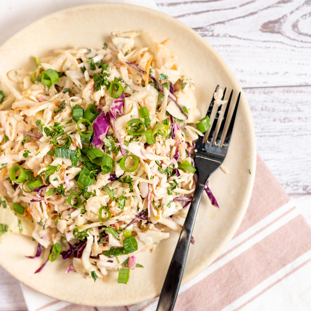 A plate of Chipotle Slaw consisting of finely shredded cabbage, green onions, and cilantro with a dressing drizzled over the top.