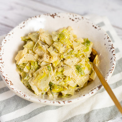 A bowl of cream braised cabbage served with a spoon, placed on a striped napkin.