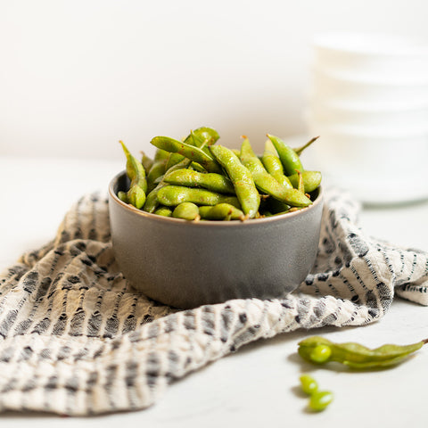 A bowl of edamame on a striped napkin, representing the product Sweet, Savory, and Spicy Edamame.