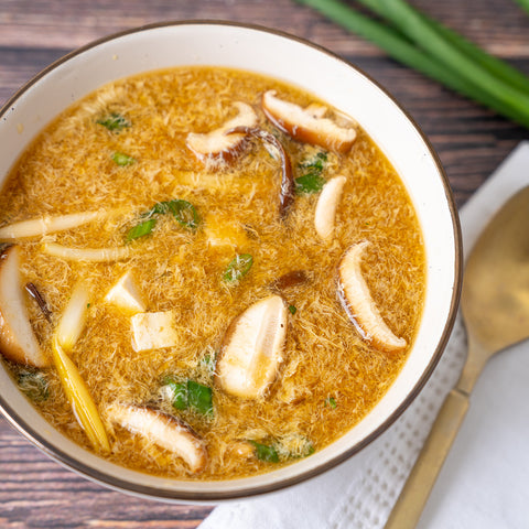 A bowl of Hot and Sour Soup with visible wood ear mushrooms, bamboo shoots, and tofu in a flavorful broth.