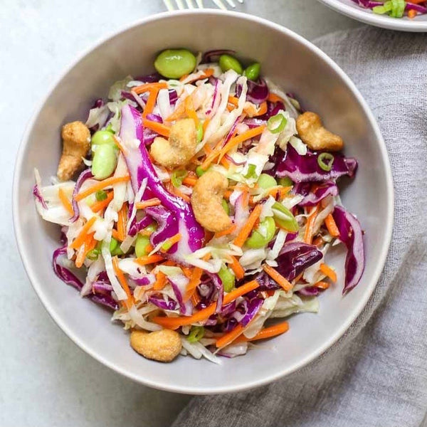 A bowl of crunchy cashew slaw with finely shredded green cabbage, cilantro, green onions, carrots, and edamame, topped with toasted cashew nuts.