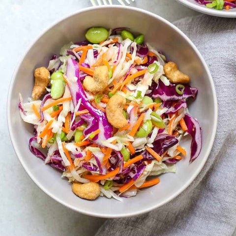 A bowl of crunchy cashew slaw with finely shredded green cabbage, cilantro, green onions, carrots, and edamame, topped with toasted cashew nuts.