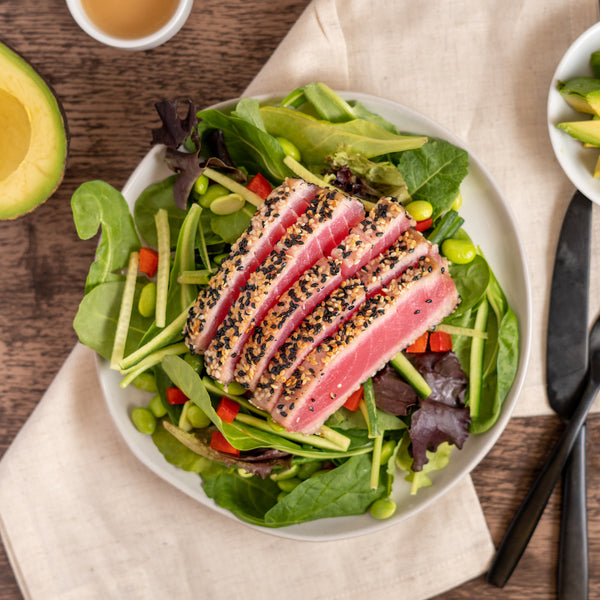 A plate of sesame crusted yellowfin tuna salad over a bed of greens with avocado and a vinaigrette dressing.