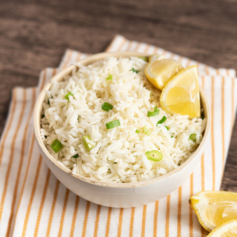 A bowl of lemon basmati rice garnished with green onions and a lemon wedge, placed on a striped napkin.