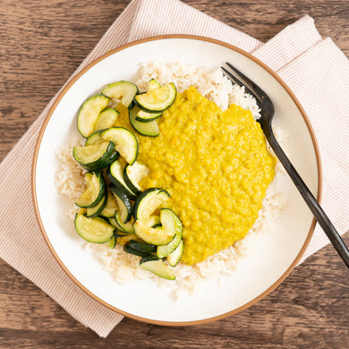 A plate containing red lentils with spices and sautéed zucchini on top, served over rice.