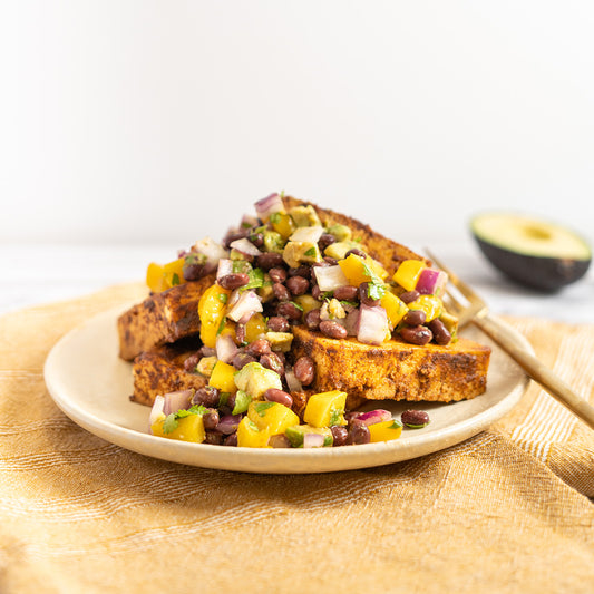 A plate of roasted tofu topped with mango avocado relish, served with slices of avocado on the side.