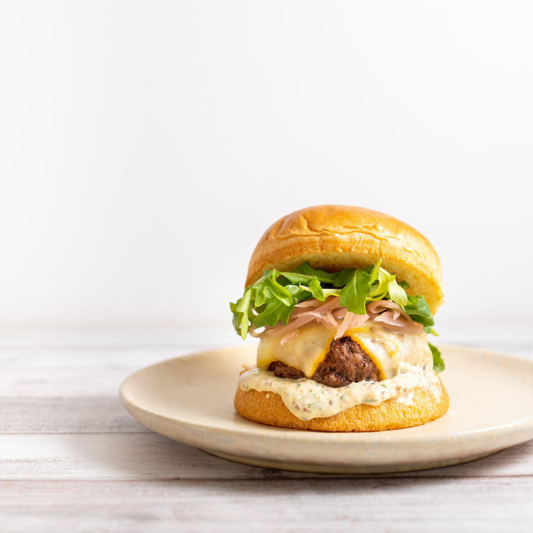A plated burger with a ground beef and pork patty, topped with cheese, onions, and lettuce, served in a bun.