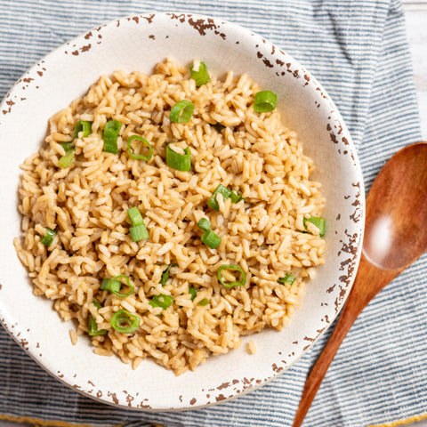 A bowl of sesame brown rice garnished with green onions, served with a wooden spoon.