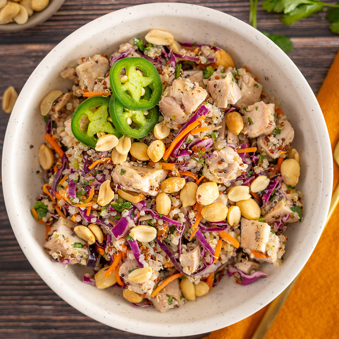 A bowl of Thai Peanut Chicken and Quinoa Salad topped with green onions and peanuts, alongside slices of jalapeno.